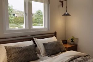 Ložnice s oknem nad postelí, které přivádí přirozené světlo do prostoru.