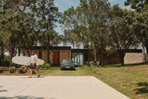 Pohled na dům ukrytý mezi stromy ukazuje příjezdovou plochu a citlivé zasazení stavby do zeleně.