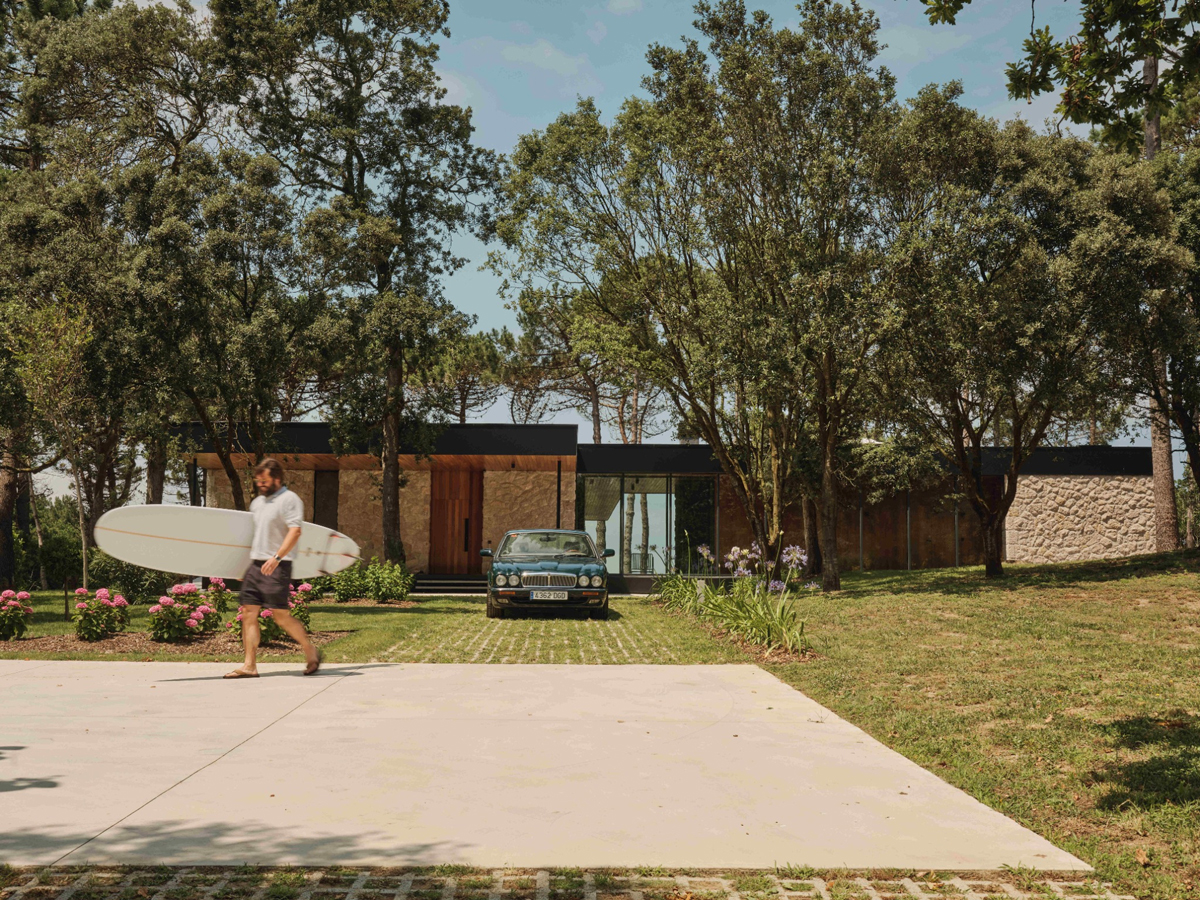 Pohled na dům ukrytý mezi stromy ukazuje příjezdovou plochu a citlivé zasazení stavby do zeleně.