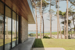 Krytá terasa a kamenná stěna rámují výhled do zahrady a směrem k moři mezi vysokými stromy.