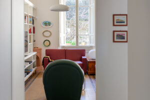 Pohled z chodby do obývací části ukazuje vysoké stropy, velké okno a barevné sezení v elegantním prostoru.