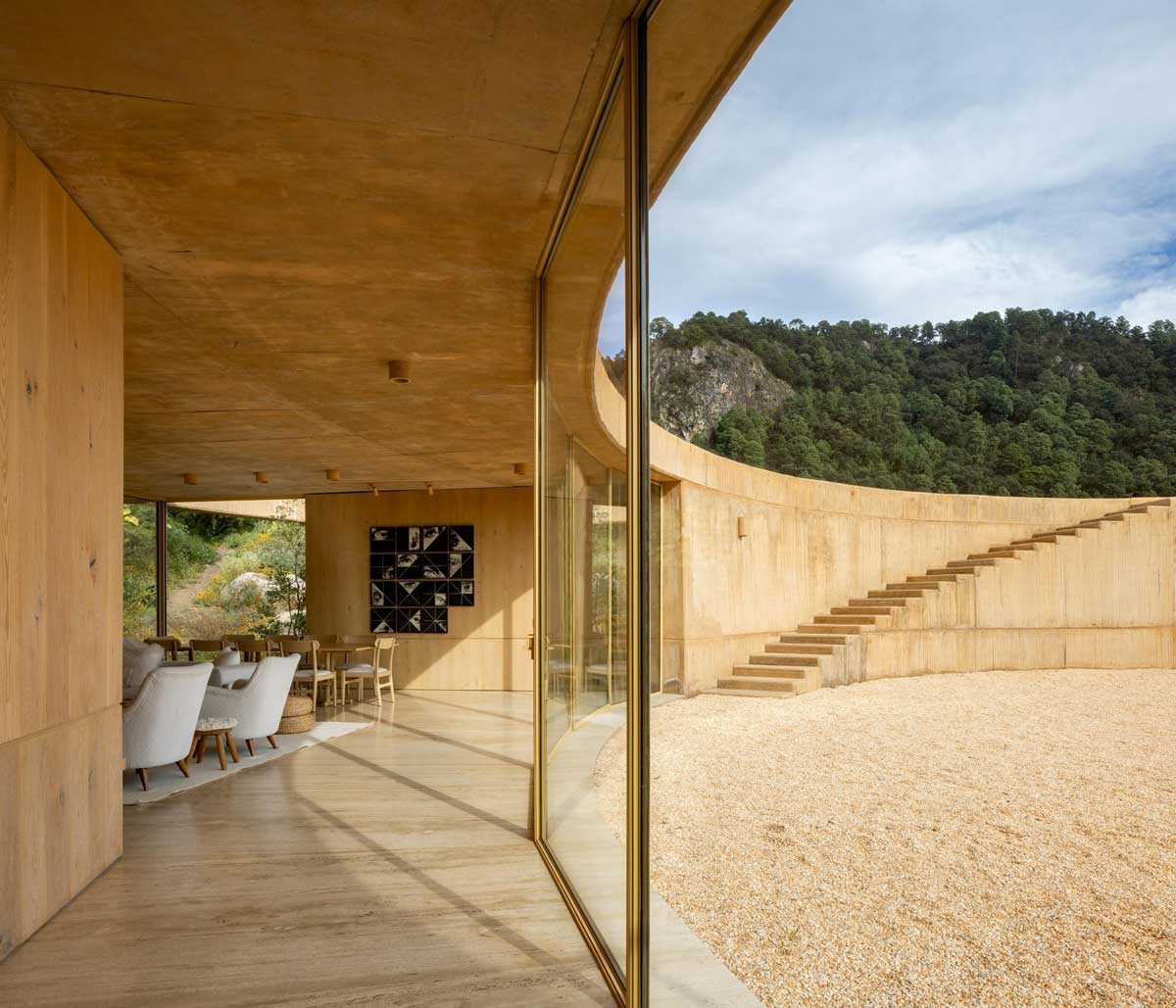 Pohled z interiéru přes prosklenou stěnu do kruhového nádvoří a okolní krajiny.