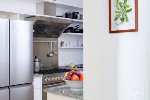 Průhled do kuchyně s nerezovými spotřebiči, žulovou deskou a ovocem na pultu působí čistě a vzdušně.