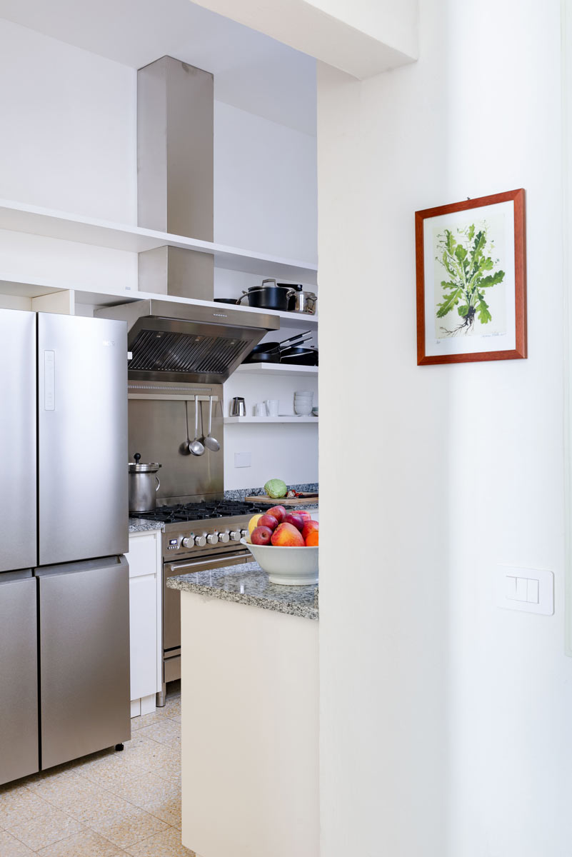 Průhled do kuchyně s nerezovými spotřebiči, žulovou deskou a ovocem na pultu působí čistě a vzdušně.