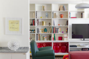 Otevřený pohled z jídelny do obývacího pokoje odhaluje vestavěnou knihovnu, zelené křeslo a výraznou červenou pohovku.