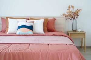 Postel s vrstvenými textiliemi a dekorativními polštáři působí luxusně ale každodenní úprava zabere čas.