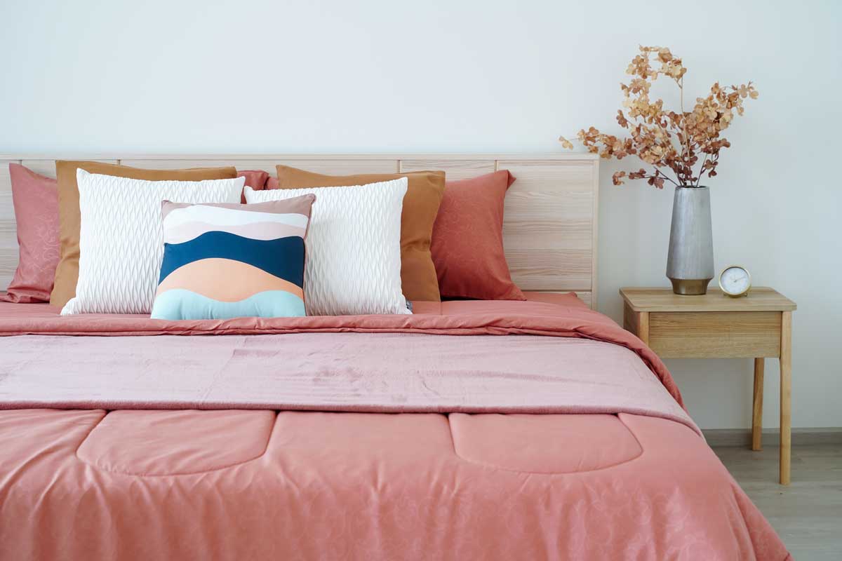 Postel s vrstvenými textiliemi a dekorativními polštáři působí luxusně ale každodenní úprava zabere čas.