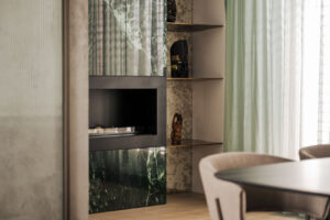 Krbová stěna v kombinaci s policemi a dekorativními prvky vytváří vizuálně zajímavé zákoutí, kde se snoubí strukturované povrchy s leskem mramoru a skla.