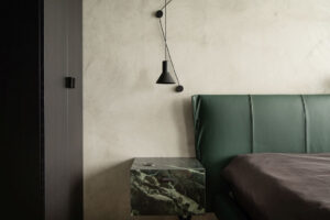 Ložnice kombinuje tmavé prvky s jemnými povrchy a mramorovým nočním stolkem, který navazuje na hlavní motiv interiéru.