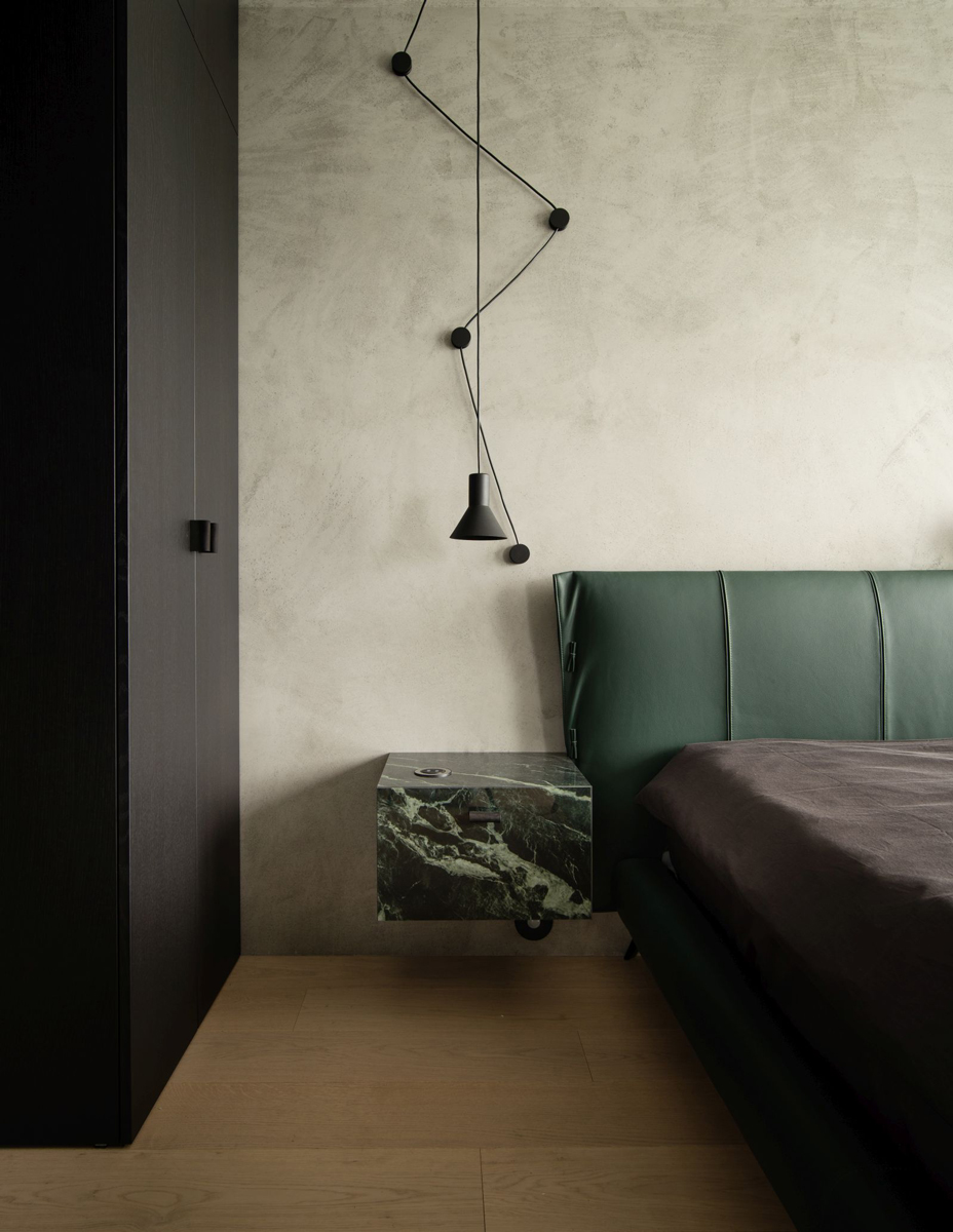 Ložnice kombinuje tmavé prvky s jemnými povrchy a mramorovým nočním stolkem, který navazuje na hlavní motiv interiéru.