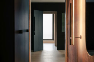 Vstupní chodba s tmavým obkladem a teplým liniovým osvětlením vytváří příjemný přechod mezi jednotlivými částmi bytu.