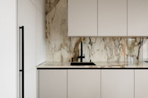 Kuchyň v jemných béžových tónech kombinuje minimalistická dvířka s výraznou mramorovou kresbou, která dodává prostoru hloubku a eleganci.