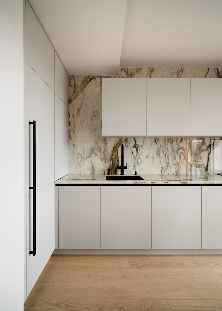 Kuchyň v jemných béžových tónech kombinuje minimalistická dvířka s výraznou mramorovou kresbou, která dodává prostoru hloubku a eleganci.