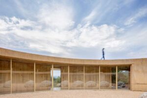 Prosklená chodba s výhledem do krajiny a jemným světlem pronikajícím dovnitř.