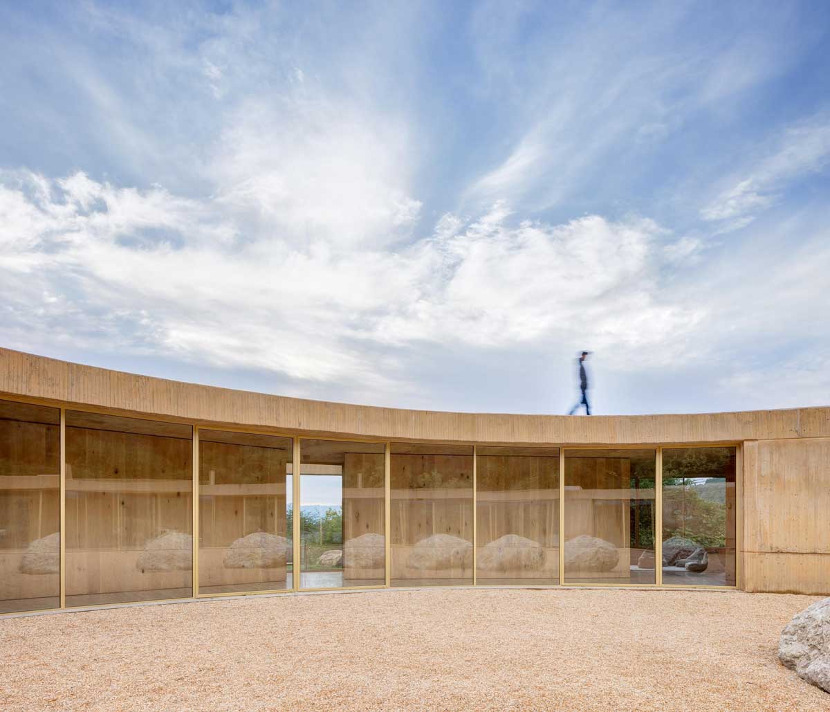 Prosklená chodba s výhledem do krajiny a jemným světlem pronikajícím dovnitř.