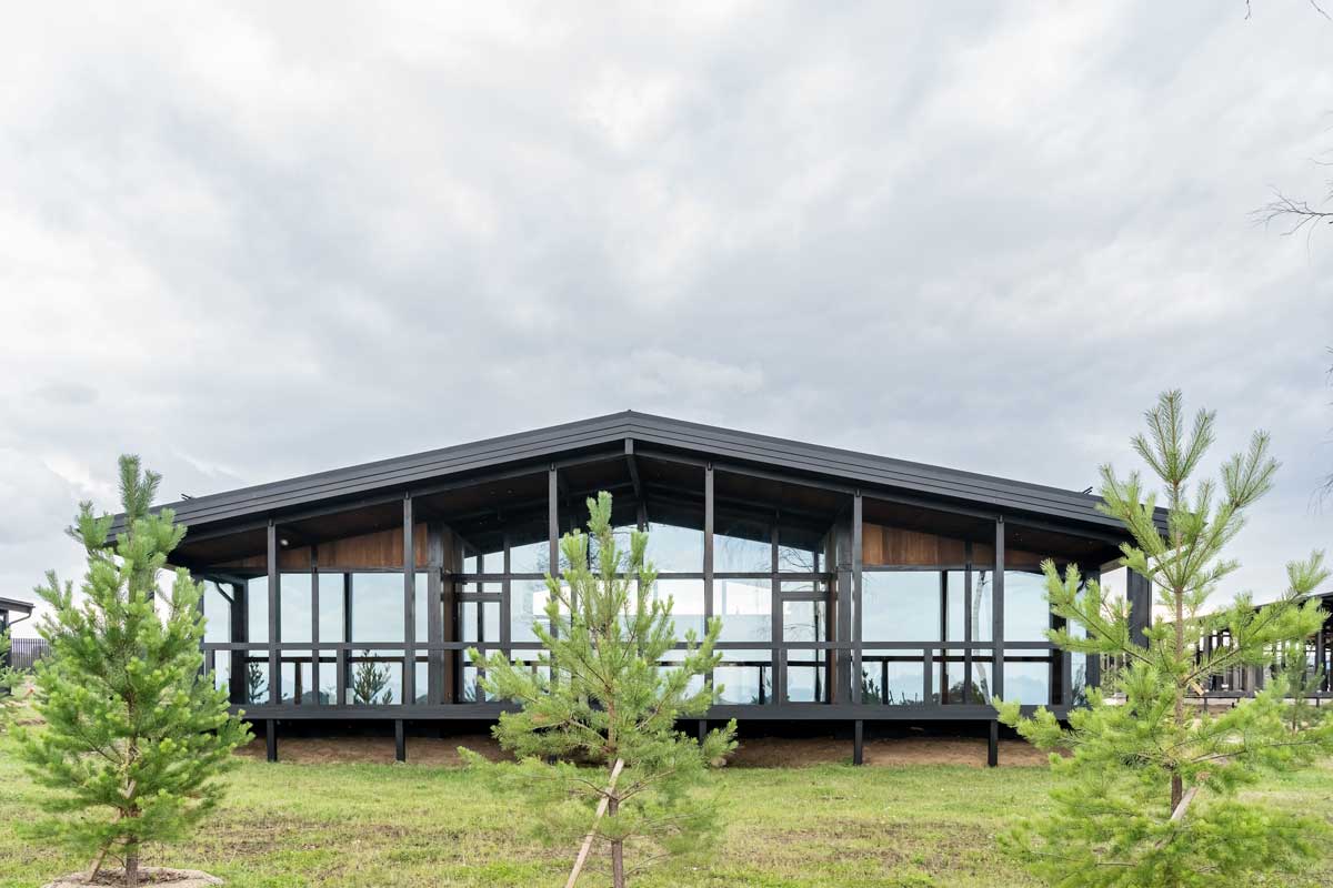 Rodinný dům s velkými prosklenými stěnami zasazený do krajiny s důrazem na propojení interiéru a exteriéru.