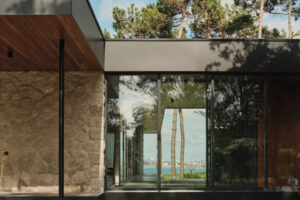 Velké prosklení vytváří průhled skrz dům až ke stromům a pobřežní krajině v dálce.