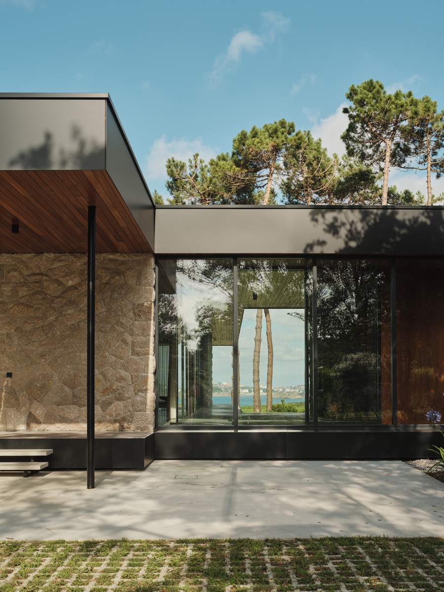 Velké prosklení vytváří průhled skrz dům až ke stromům a pobřežní krajině v dálce.