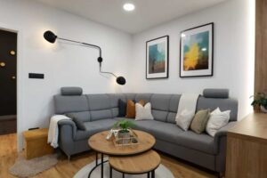 Rohová sedačka v neutrálních tónech doplněná dekorativními polštáři vytváří útulné místo pro odpočinek.