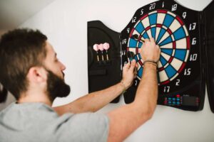 Muž hraje šipky ve svém koutě který je přizpůsobený pro aktivní odpočinek a zábavu.