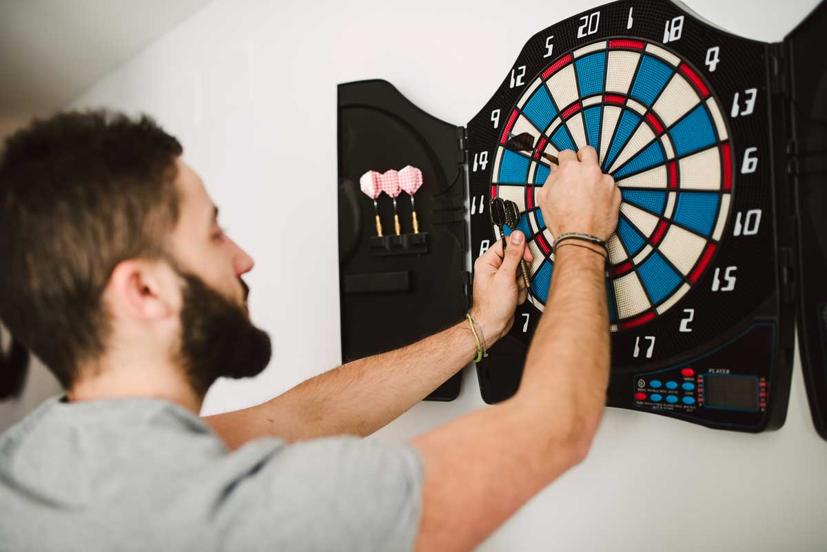 Muž hraje šipky ve svém koutě který je přizpůsobený pro aktivní odpočinek a zábavu.