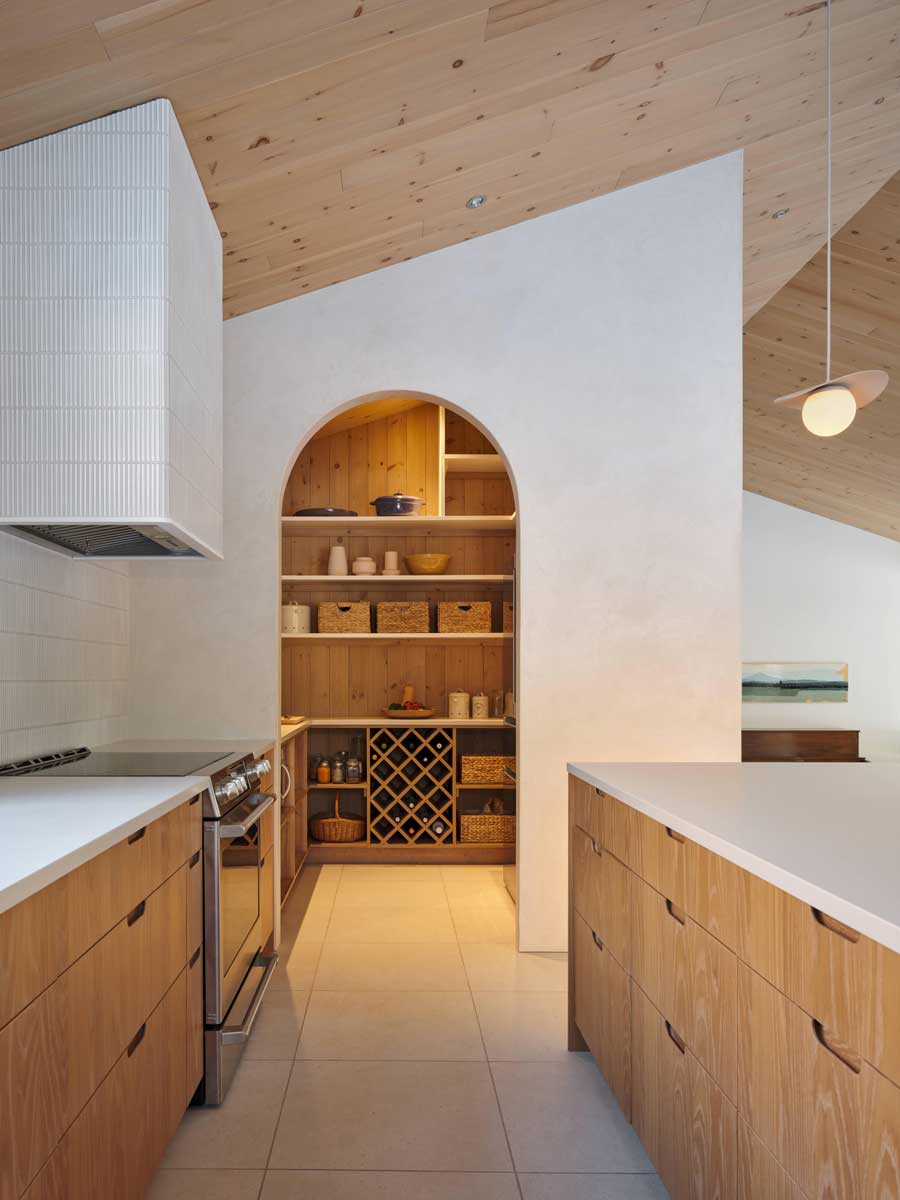 Kuchyň s dřevěnou linkou a obloukovým vstupem do spíže s otevřenými policemi a úložnými koši