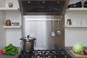 Čelní pohled na profesionální sporák s šesti hořáky, dvojitou troubou a nerezovým odsavačem v centru kuchyně.