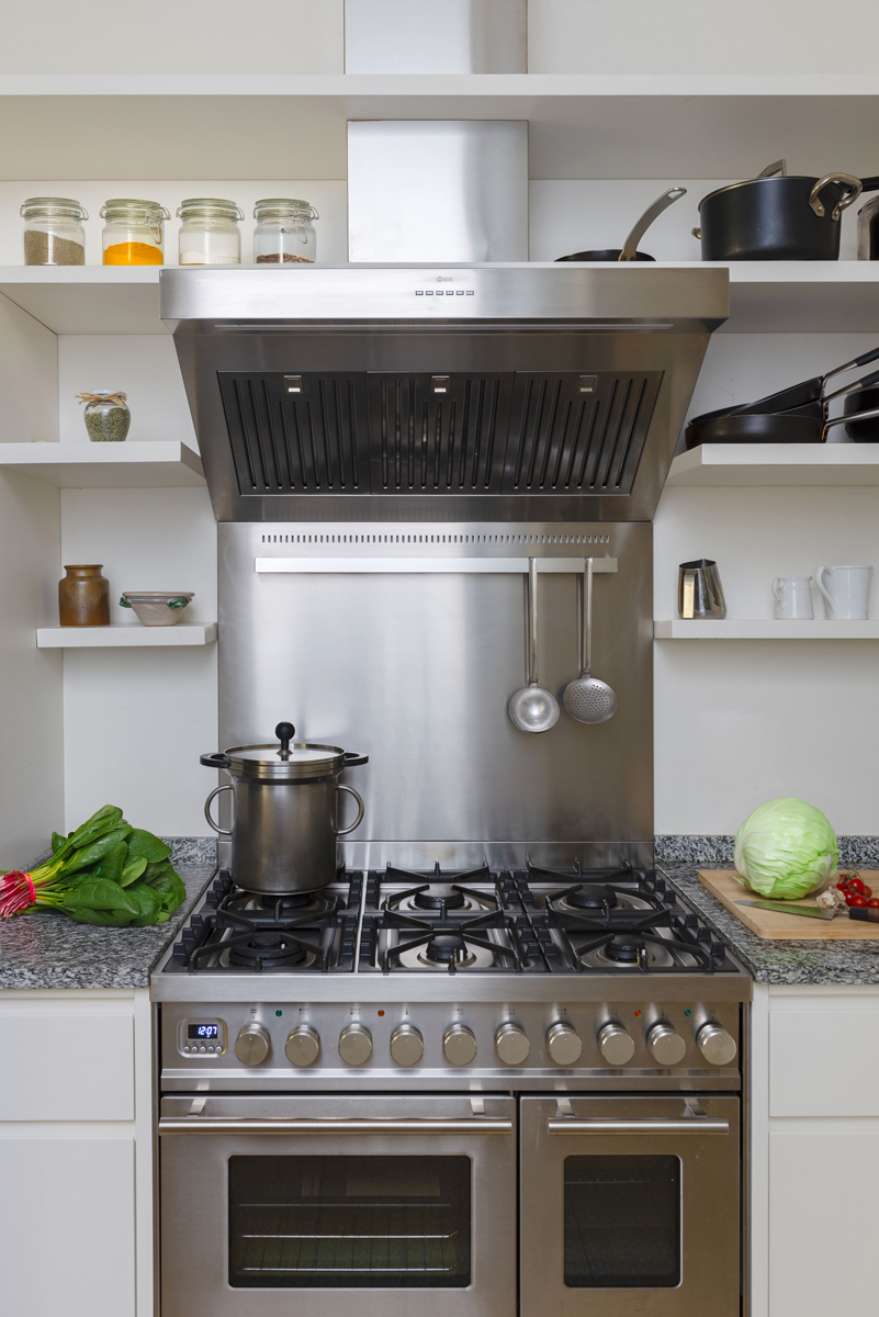 Čelní pohled na profesionální sporák s šesti hořáky, dvojitou troubou a nerezovým odsavačem v centru kuchyně.