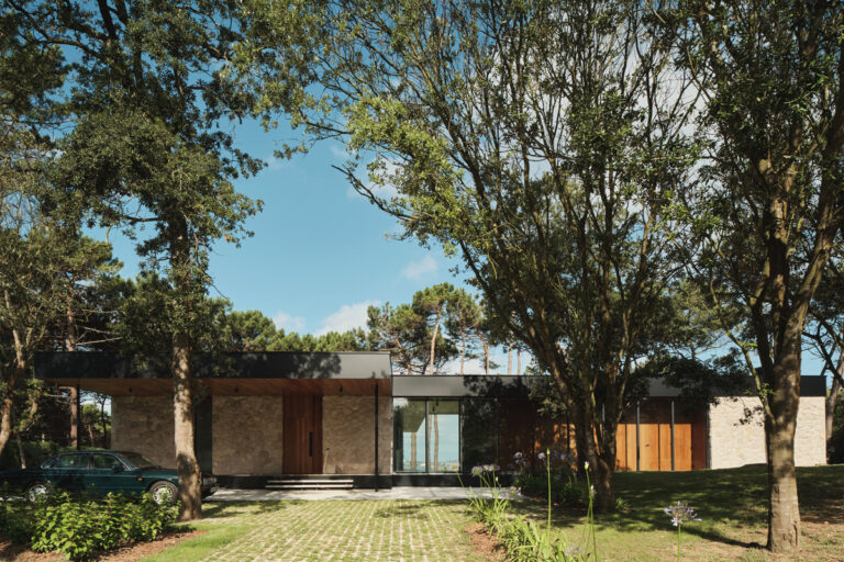 Pohled na přední fasádu domu mezi vzrostlými stromy zdůrazňuje klidné zasazení stavby do přírody.