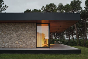 Večerní pohled na prosklený roh domu ukazuje osvětlený interiér a krytou terasu obrácenou do zahrady.