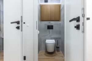 Moderní toaleta v šedém dekoru s černými detaily a dřevěnou skříňkou působí elegantně a sjednoceně.