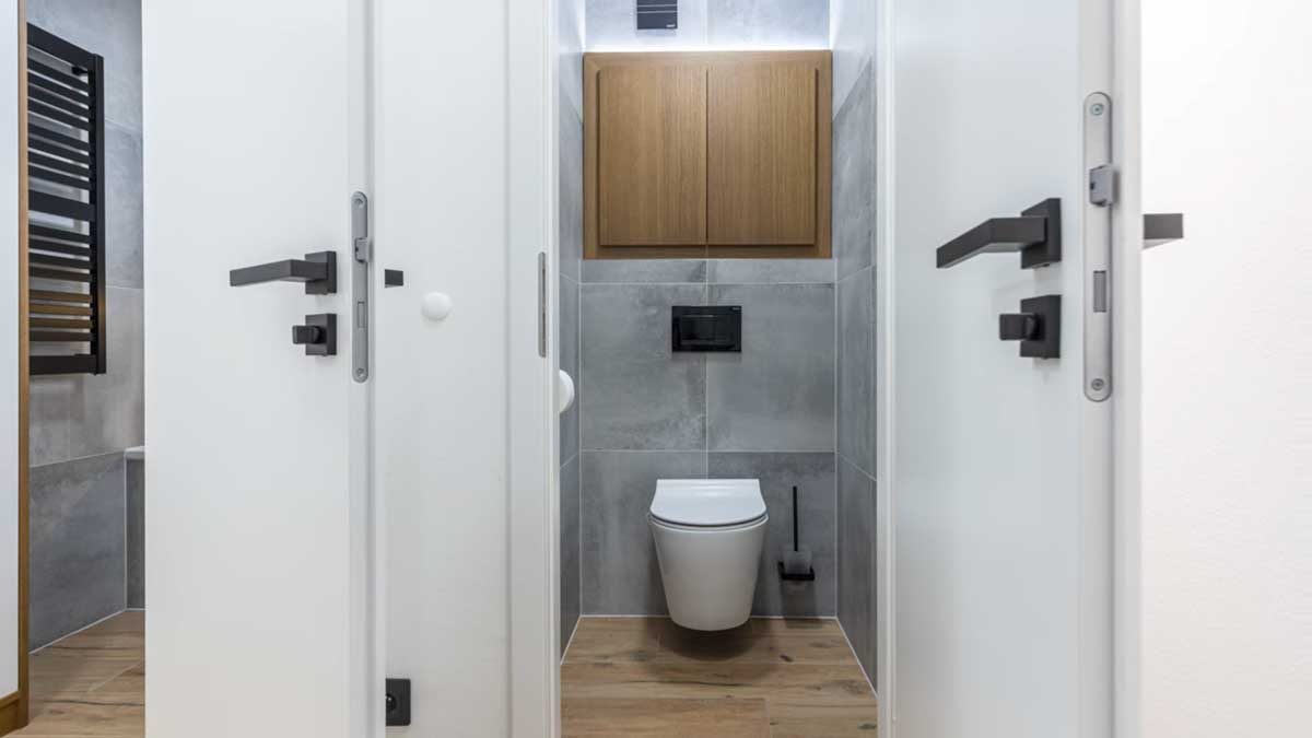 Moderní toaleta v šedém dekoru s černými detaily a dřevěnou skříňkou působí elegantně a sjednoceně.