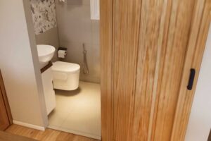 Koupelna v tiny house s toaletou, umyvadlem a posuvnými dřevěnými dveřmi.