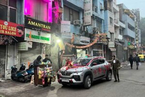 Ulice v Dillí s obchody, neonovými světly a ozdobeným autem projíždějícím městem.