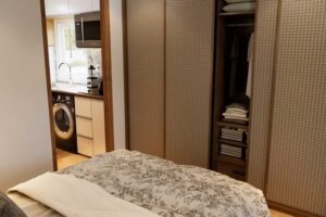 Ložnice v tiny house s vestavěnou skříní a výhledem do kuchyňské části.