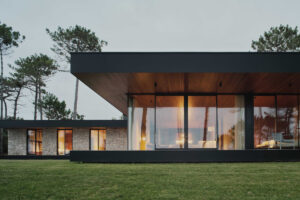 Velkoformátová okna propojují hlavní obytný prostor se zahradou a otevírají výhled mezi stromy.