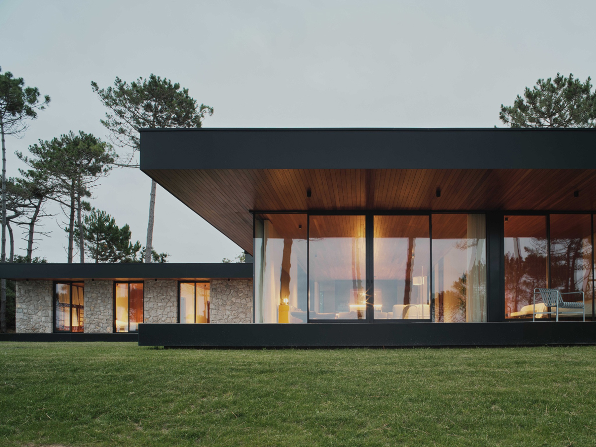 Velkoformátová okna propojují hlavní obytný prostor se zahradou a otevírají výhled mezi stromy.