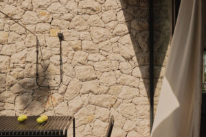 Kryté venkovní posezení s kamennou stěnou a jednoduchým nábytkem nabízí chráněné místo k odpočinku.