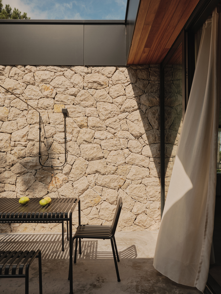 Kryté venkovní posezení s kamennou stěnou a jednoduchým nábytkem nabízí chráněné místo k odpočinku.