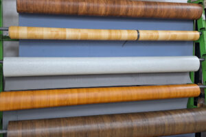 Vzorky vinylových podlah v různých dekorech dřeva a kamene vystavené na stojanu v prodejně.