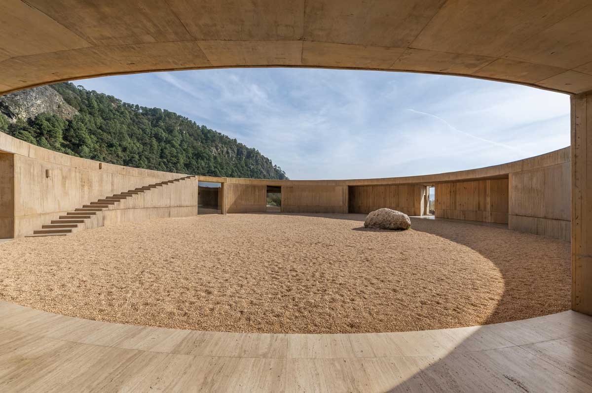 Kruhové vnitřní nádvoří s kamenným povrchem a minimalistickou architekturou kolem.