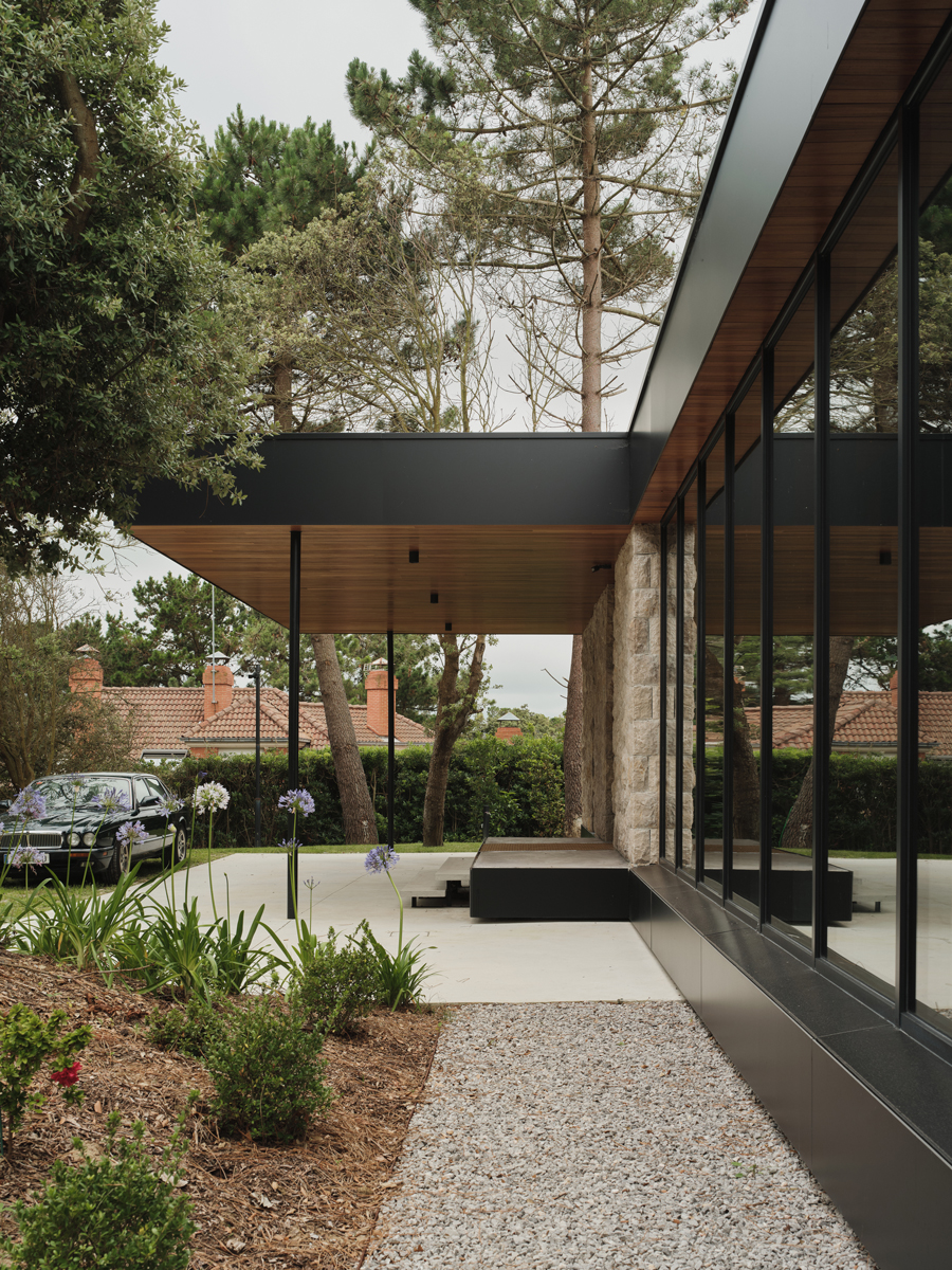 Vstupní část domu s dlouhým přesahem střechy, prosklenou fasádou a upravenou zahradou působí elegantně a klidně.