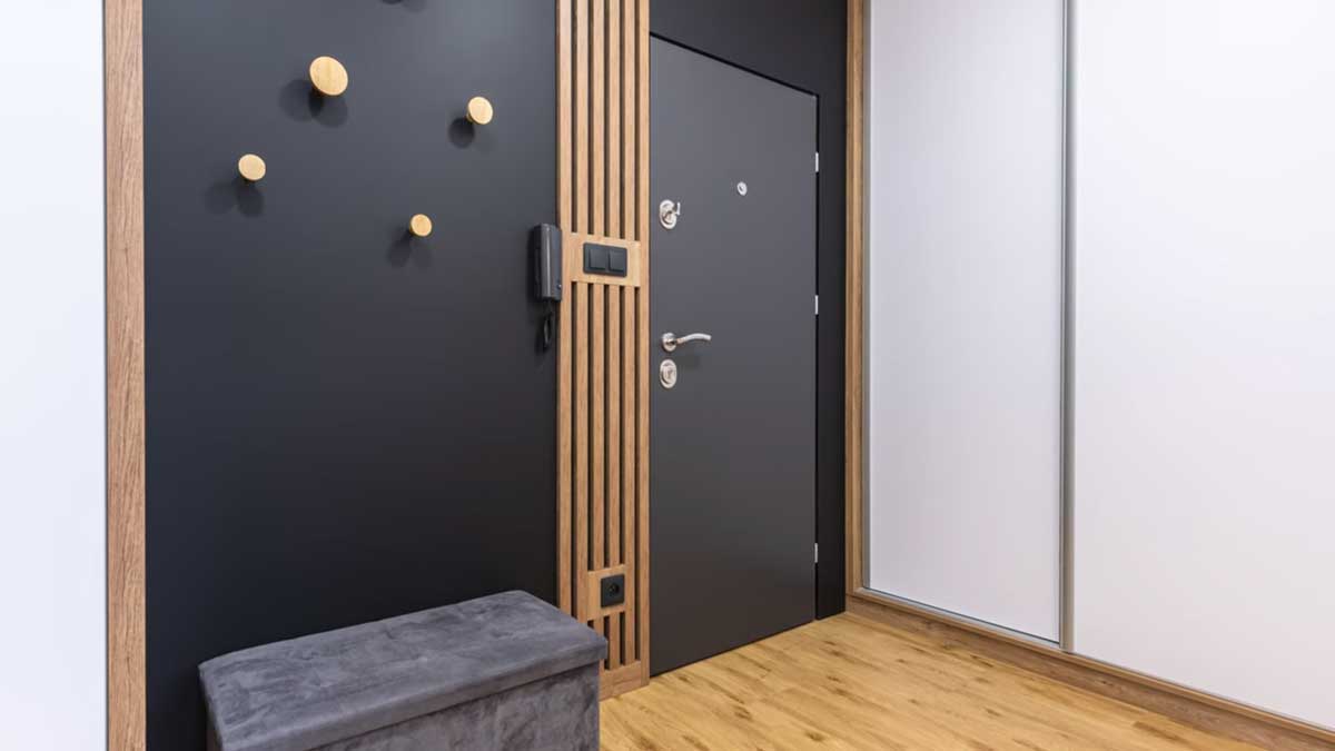 Vstupní prostor s černou stěnou dřevěnými lamelami a vestavěnými skříněmi působí elegantně a organizovaně.