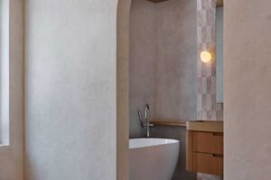 Obloukový průchod z ložnice do koupelny s volně stojící vanou a jemnými přírodními materiály