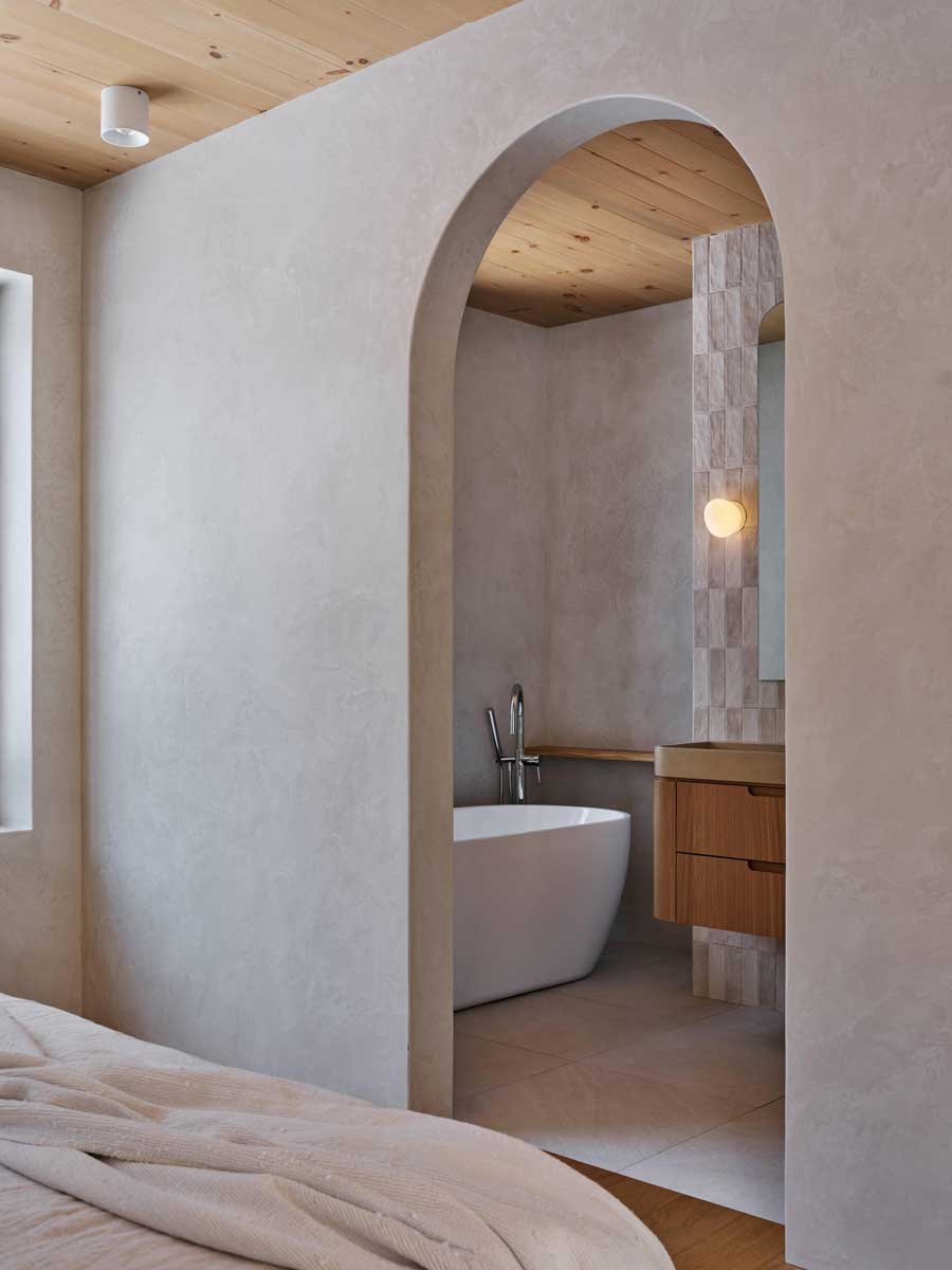 Obloukový průchod z ložnice do koupelny s volně stojící vanou a jemnými přírodními materiály