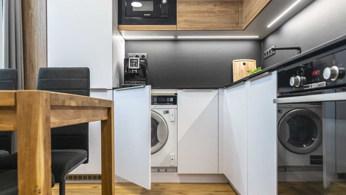 Pračka nenápadně ukrytá v kuchyňské lince zachovává čistý vzhled prostoru a nenarušuje design interiéru.