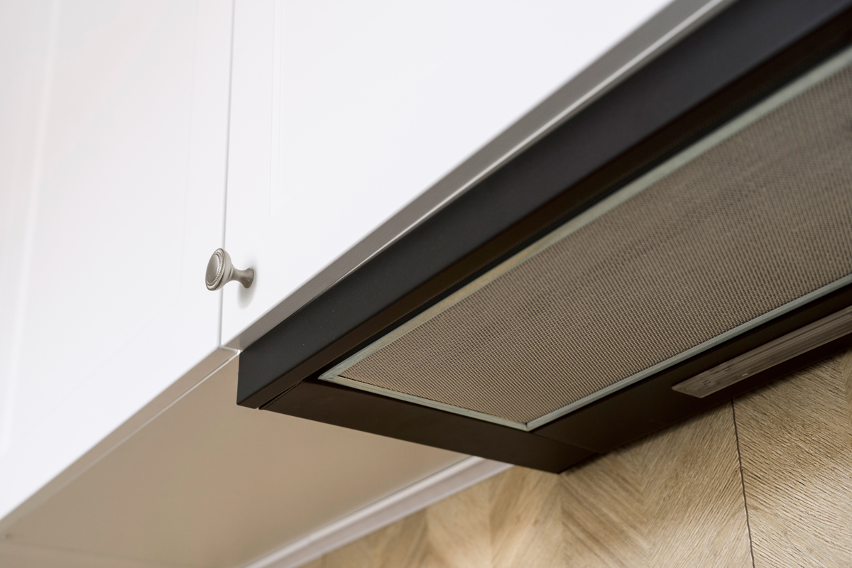 Vestavný odsavač par ukrytý v horní skříňce nabízí nenápadné řešení pro moderní kuchyně s čistými liniemi.