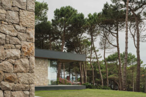 Boční pohled na kamennou fasádu domu ukazuje terasu, pečlivě udržovaný trávník a vzrostlé stromy v okolí.