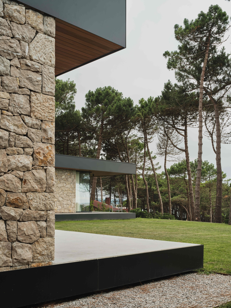 Boční pohled na kamennou fasádu domu ukazuje terasu, pečlivě udržovaný trávník a vzrostlé stromy v okolí.