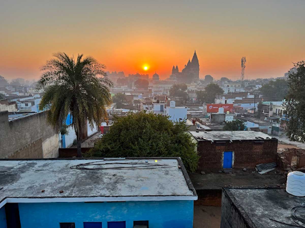 Východ slunce nad indickým městem s palmou v popředí a chrámem na horizontu.